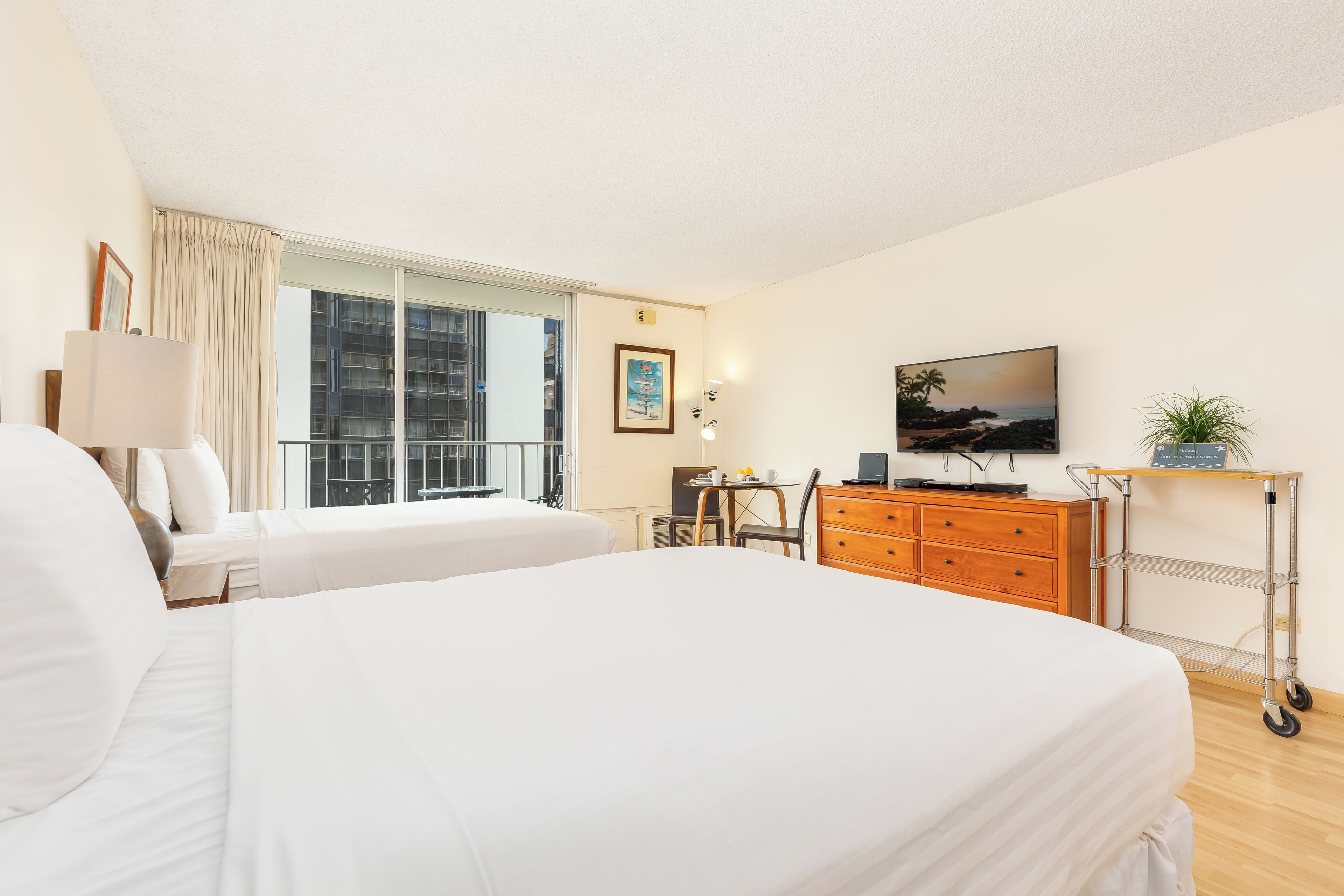 A hotel room with two beds, a desk with a chair, a television, and a small table with a plant.
