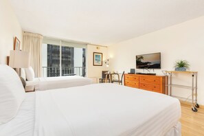 Ein Hotelzimmer mit zwei Betten, einem Schreibtisch mit Stuhl, einem Fernseher und einem kleinen Tisch mit Pflanze.