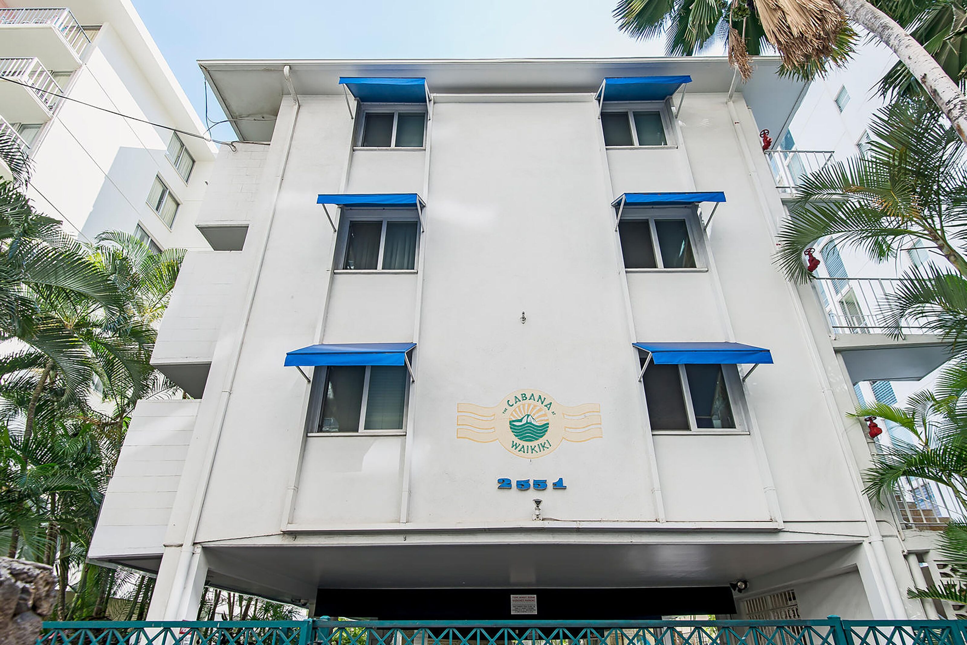 Ein mehrstöckiges Gebäude mit weißer Fassade und blauen Markisen, mit einem Logo und der Nummer 2551.