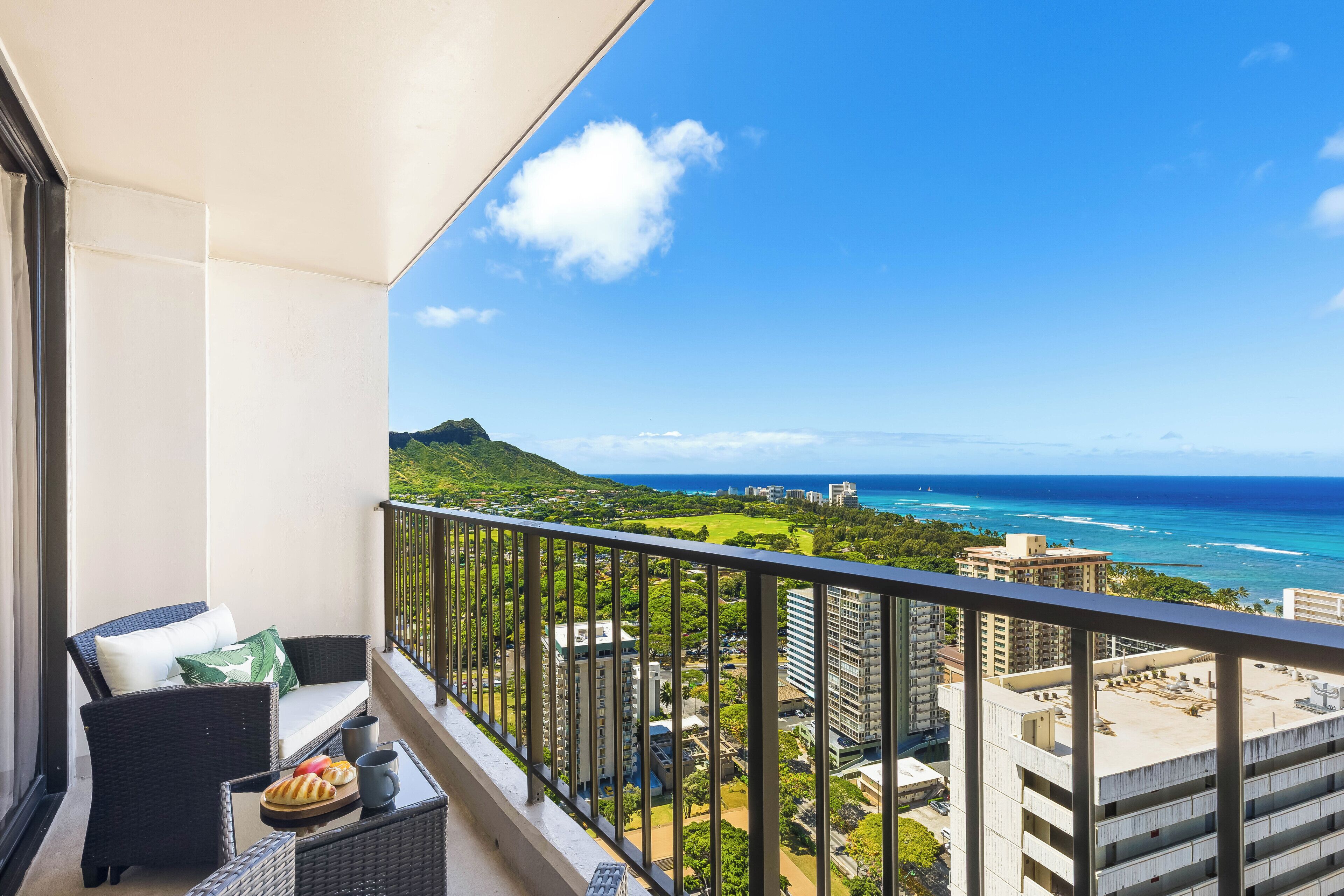 A balcony with wicker furniture, a view of the ocean, and buildings in the distance.