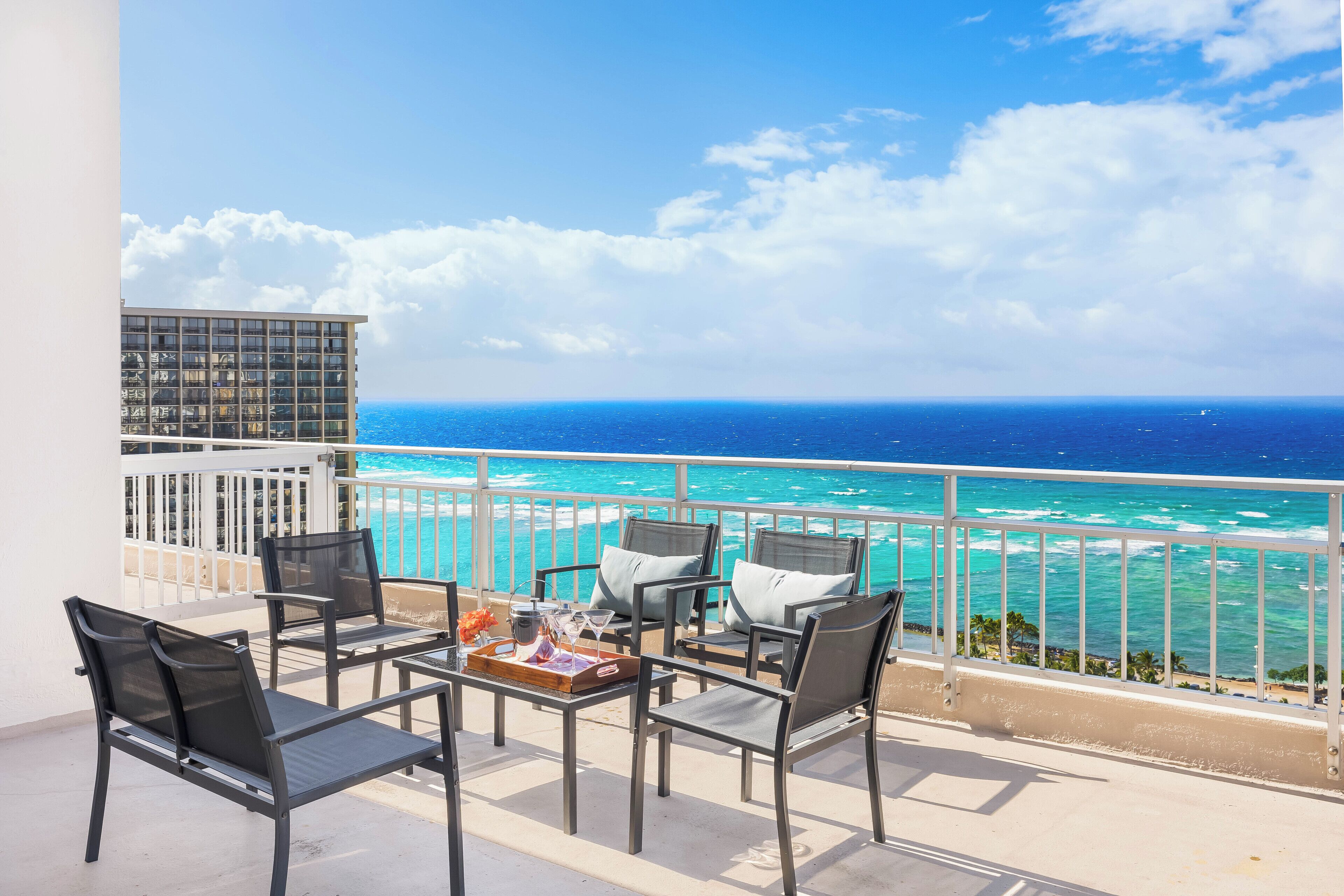 A balcony with a view of the ocean, equipped with chairs and a table.