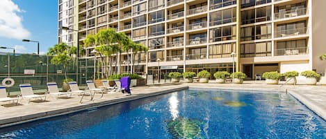 A hotel with a swimming pool, multiple balconies, and outdoor seating areas.
