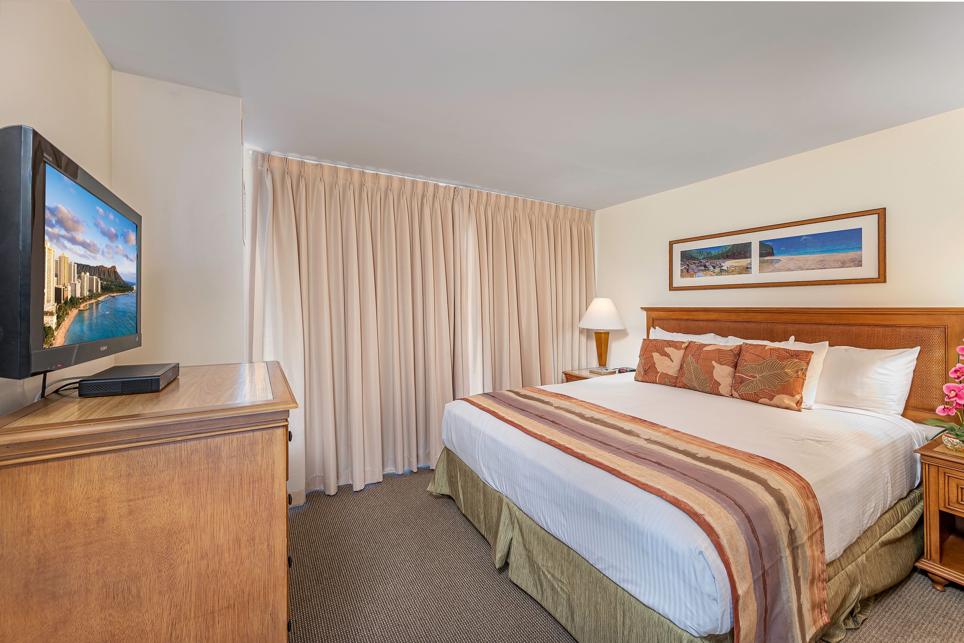 A hotel room with a bed, a television, a lamp, and a painting on the wall.