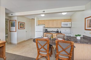 A modern kitchen with wooden cabinets, a microwave, and a dining area with a table and chairs. - MT & Golf Course Views Waikiki Sunset by the Beach W/full Kitchen & Wifi (Honolulu)