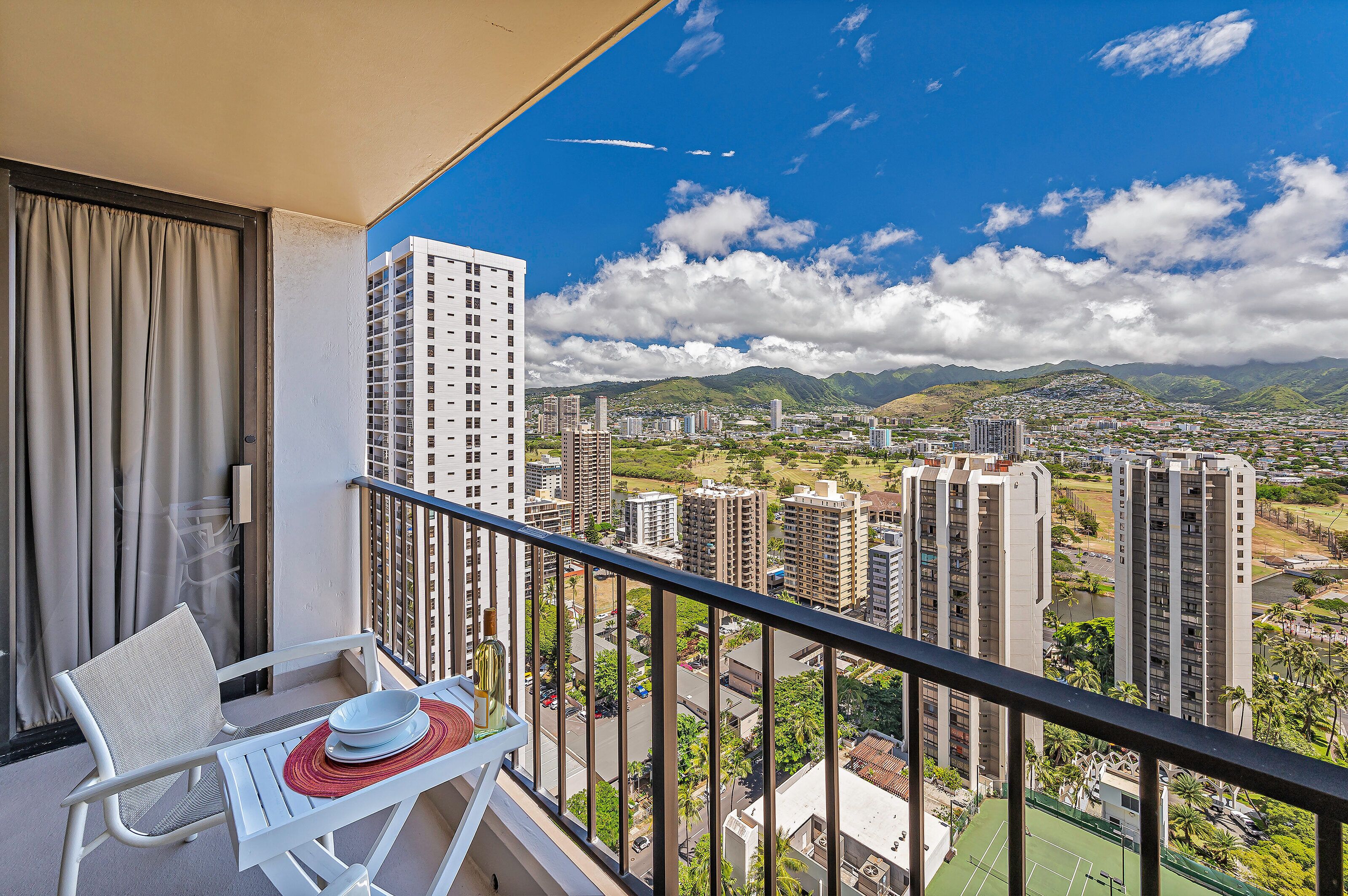 A balcony with a view of a cityscape, including high-rise buildings and mountains.