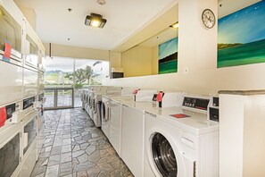 A laundry room with multiple washing machines, a stone-tiled floor, and a view through the glass door. - Ocean-diamond Head Waikiki Condo at Island Colony Short Walk to the Beach (Honolulu)