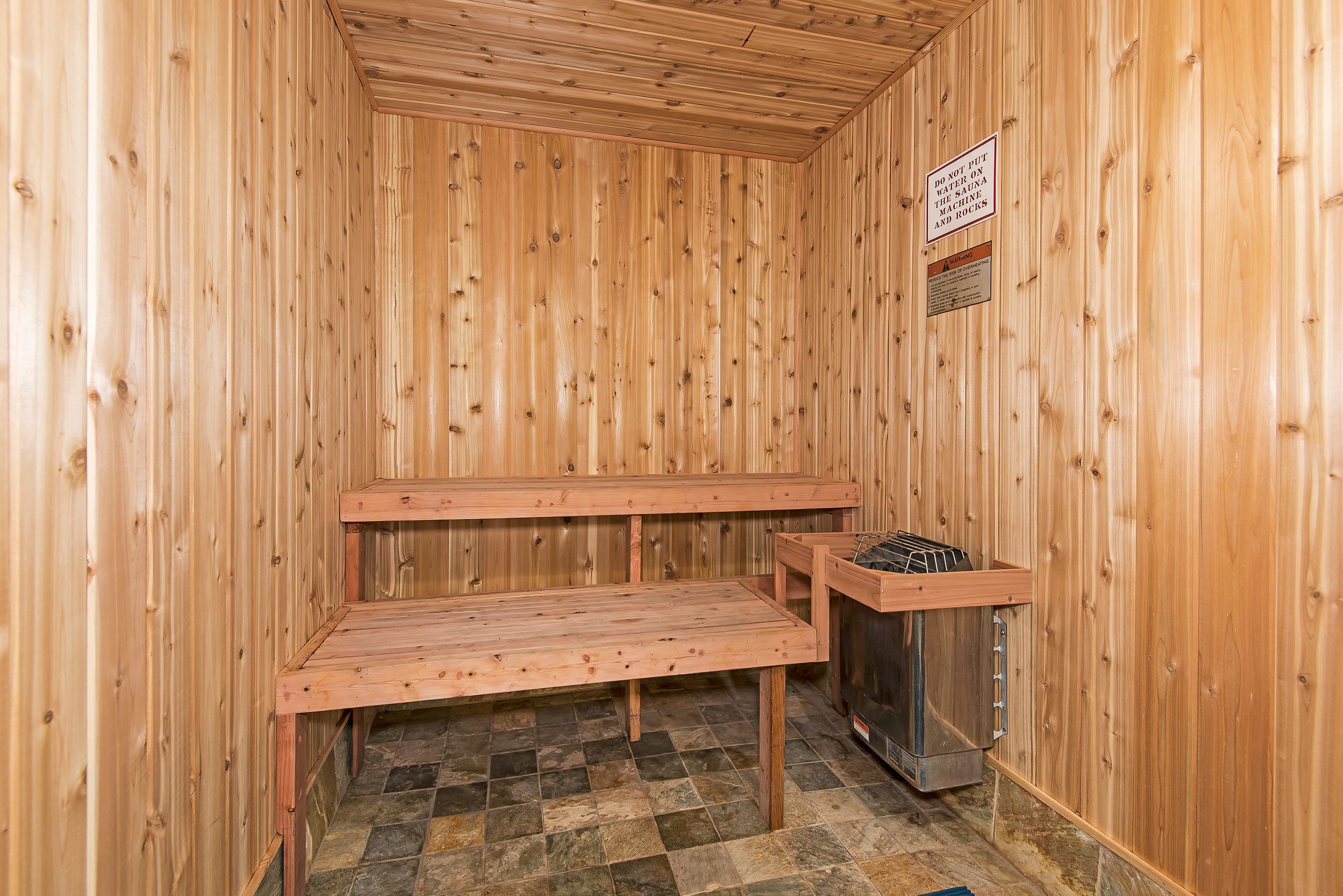 A sauna room with wooden walls and benches, a stone-tiled floor, and a sauna unit.
