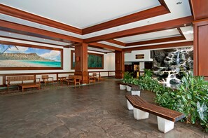 A lobby with wooden benches, a large painting of a beach, and a waterfall display. - Mountain and City Tropical Condo at Waikiki Banyan Half a Block to the Beach (Honolulu)