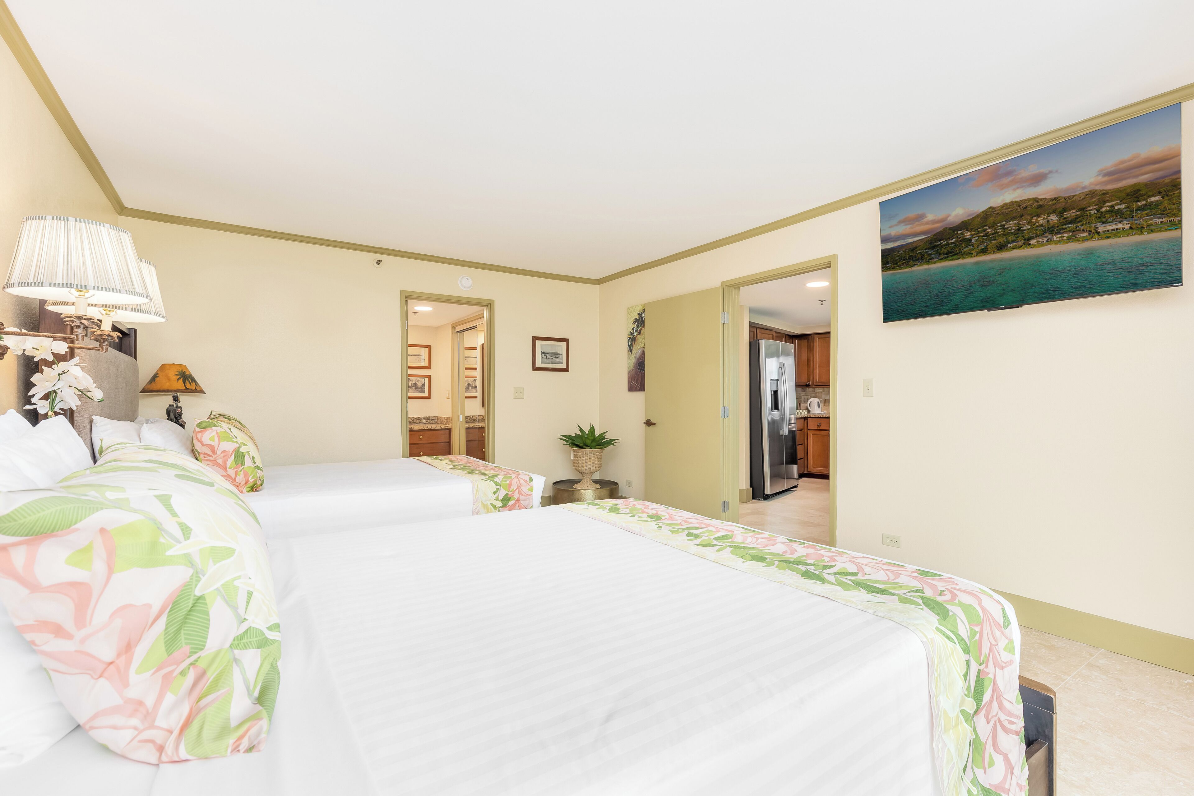 Une chambre d’hôtel avec deux lits, un tableau représentant une plage, une plante et une porte donnant sur une salle de bain.