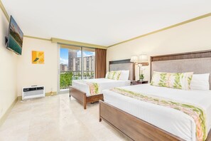 Ein Hotelzimmer mit zwei Betten, einem Fernseher, einer Heizung, einem Fenster mit Blick auf Gebäude und einer Lampe.