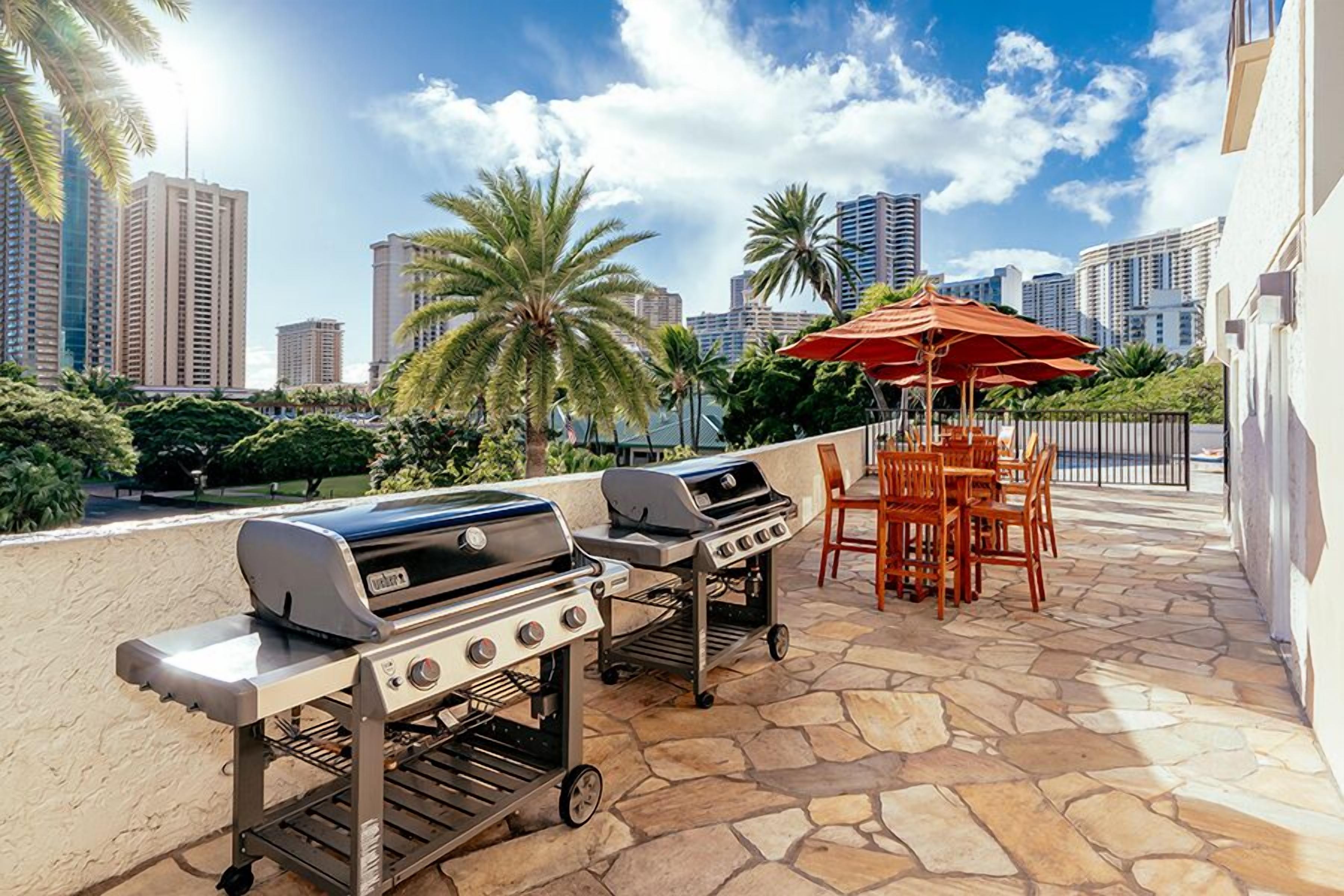 An outdoor patio with two barbecue grills, a table with chairs, and an umbrella.
