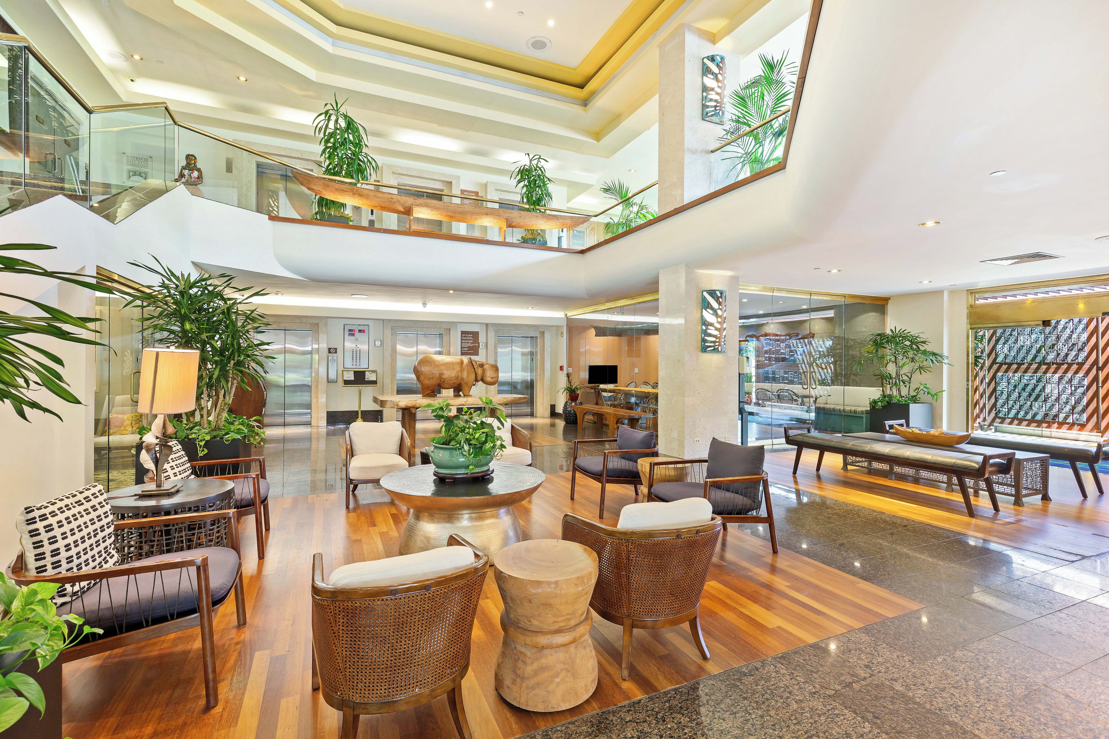 A spacious lobby with a high ceiling, multiple seating areas, and a central plant arrangement.