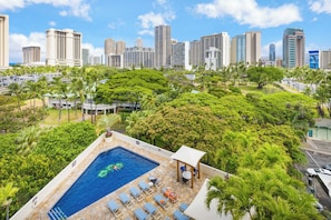 A rooftop pool with lounge chairs, surrounded by lush greenery and a city skyline in the background. - Luana at Waikiki 1-bed Ocean View Getaway in the Heart of Waikiki (Honolulu)