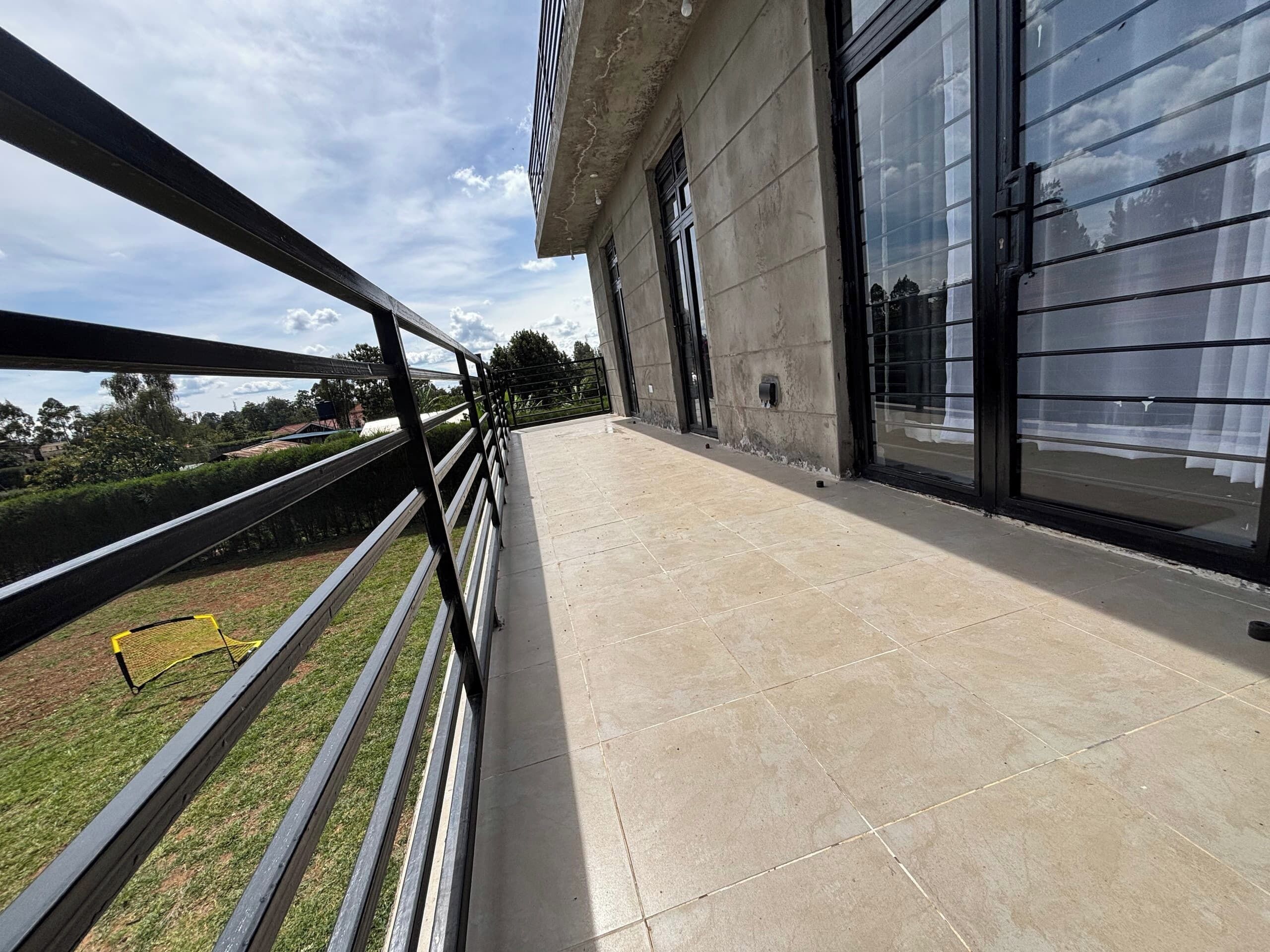 Een balkon met een metalen hekwerk, een geplaveid terras en uitzicht op een gebouw met grote ramen.