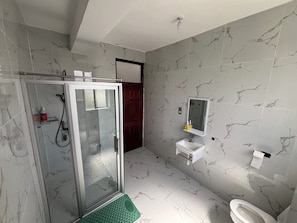 Un baño moderno con ducha de vidrio, inodoro y lavamanos con espejo.