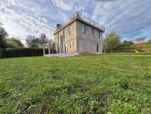 A modern two-story house with a flat roof and a balcony, surrounded by a well-maintained lawn.