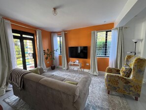 Una sala de estar con sofá, sillón, televisor y una planta en maceta.