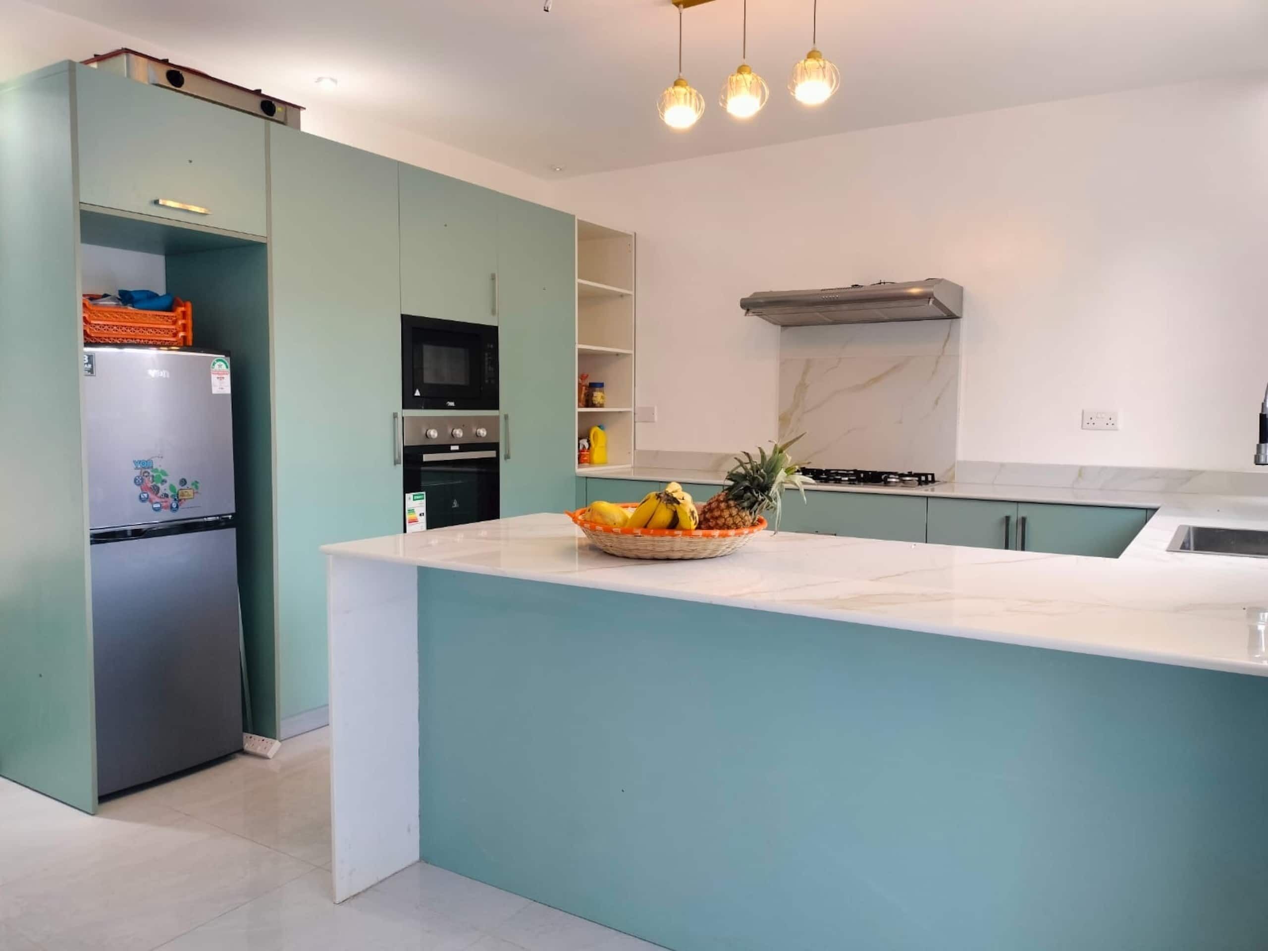 Een moderne keuken met een centraal eiland, inbouwapparatuur en hanglampen.