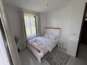 A bedroom with a bed, a bedside table, a window with curtains, and a rug.