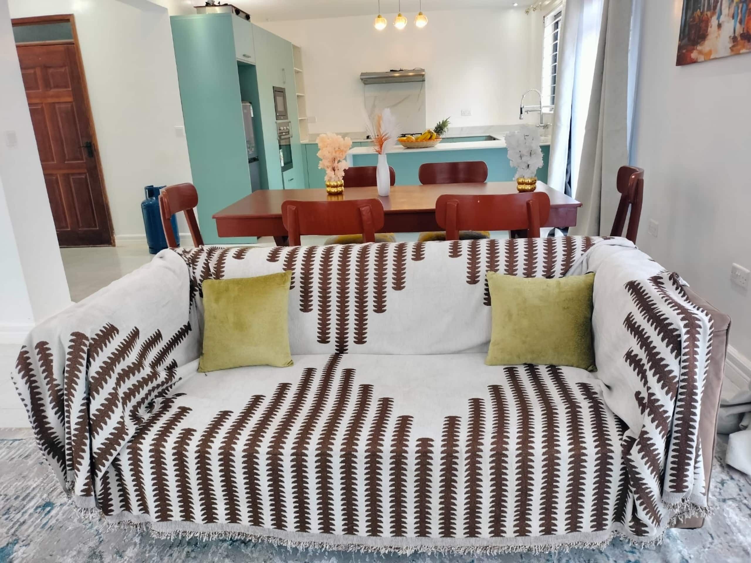 Un soggiorno con un divano a motivi, un tavolo da pranzo con sedie e una cucina sullo sfondo.