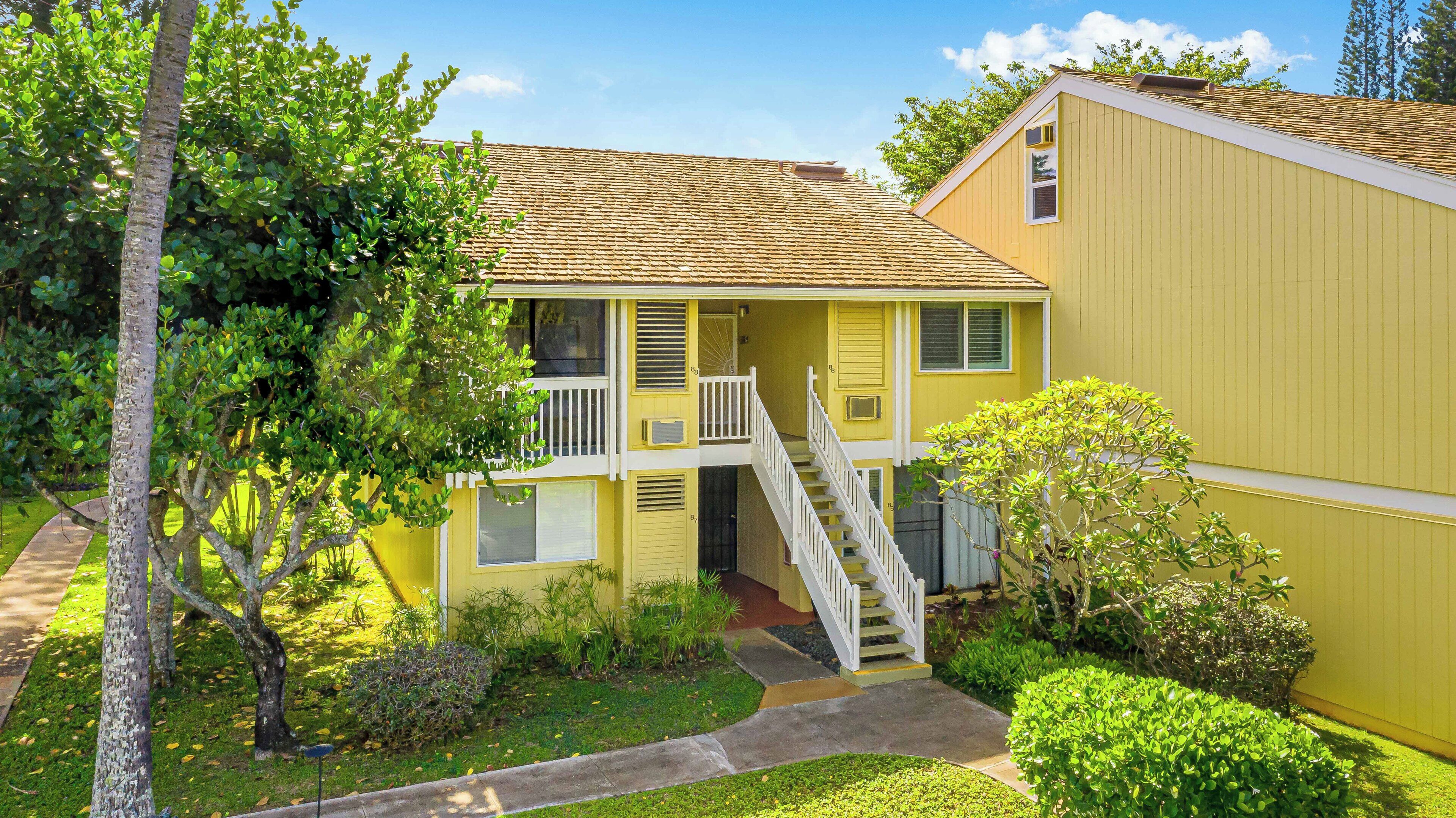 A two-story yellow house with a front porch, a staircase, and a small garden area.
