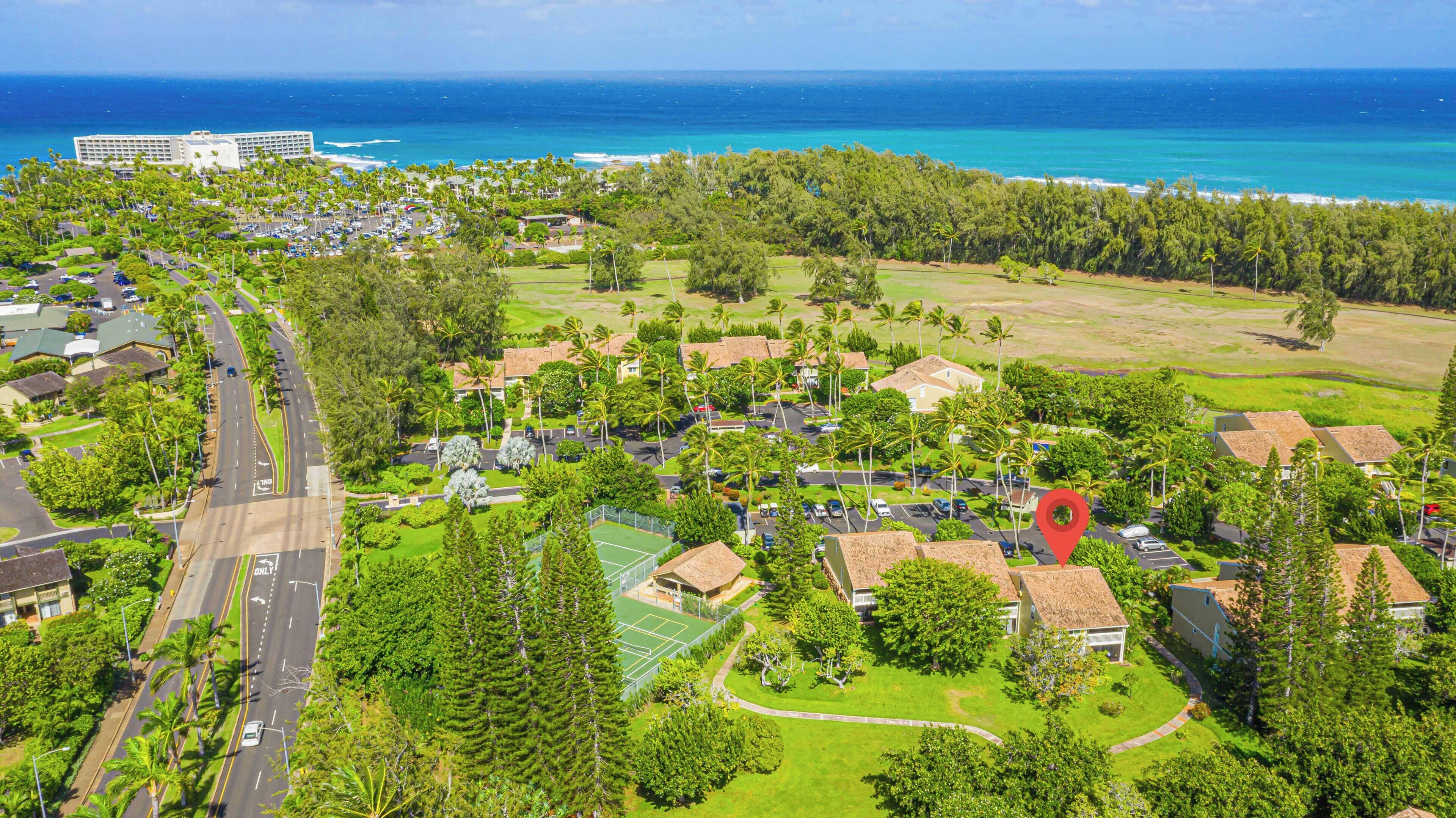An aerial view of a coastal residential area with houses, a road, and a large hotel.