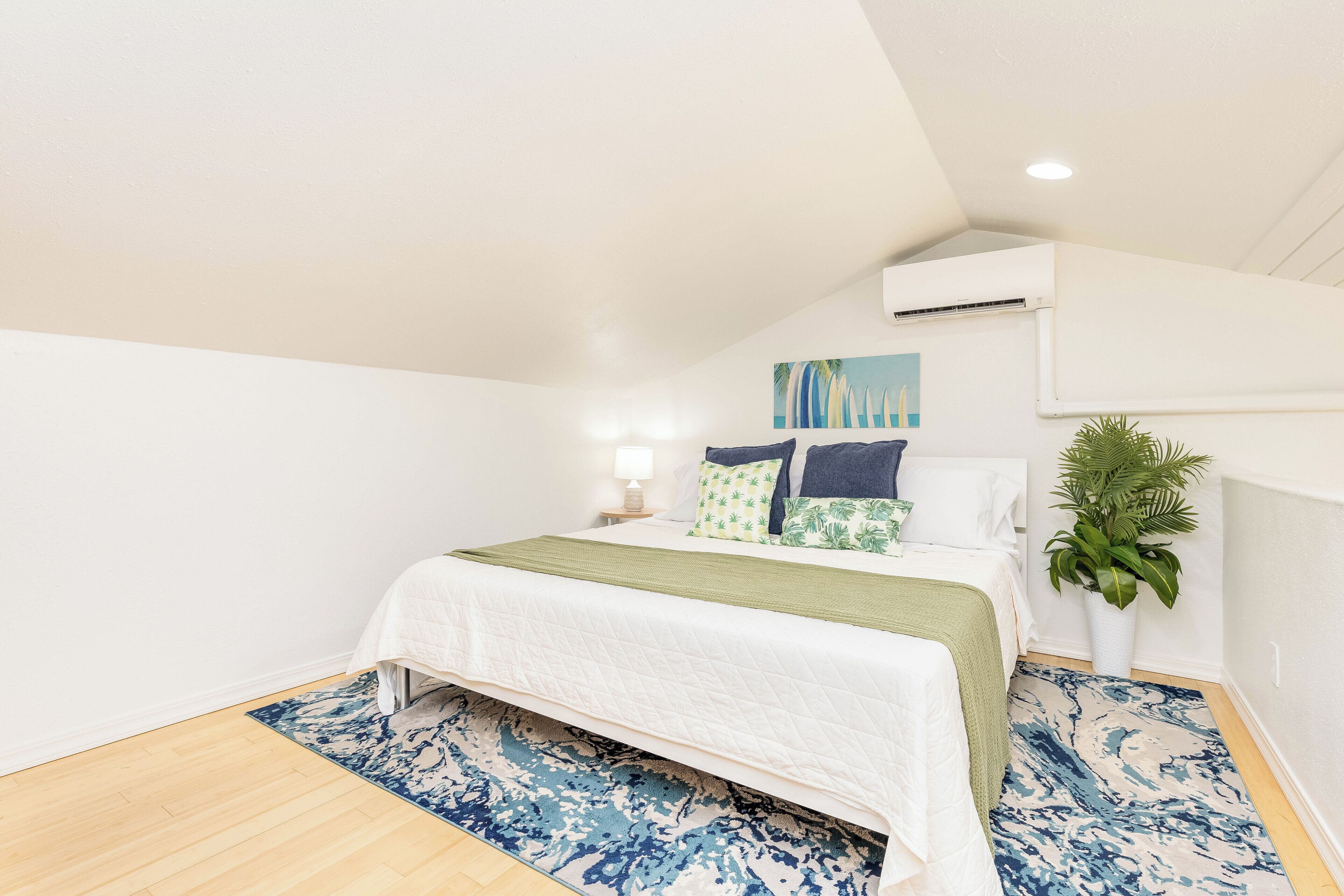Une chambre à coucher avec un lit, une table de chevet, une lampe, une plante et un ventilateur de plafond.