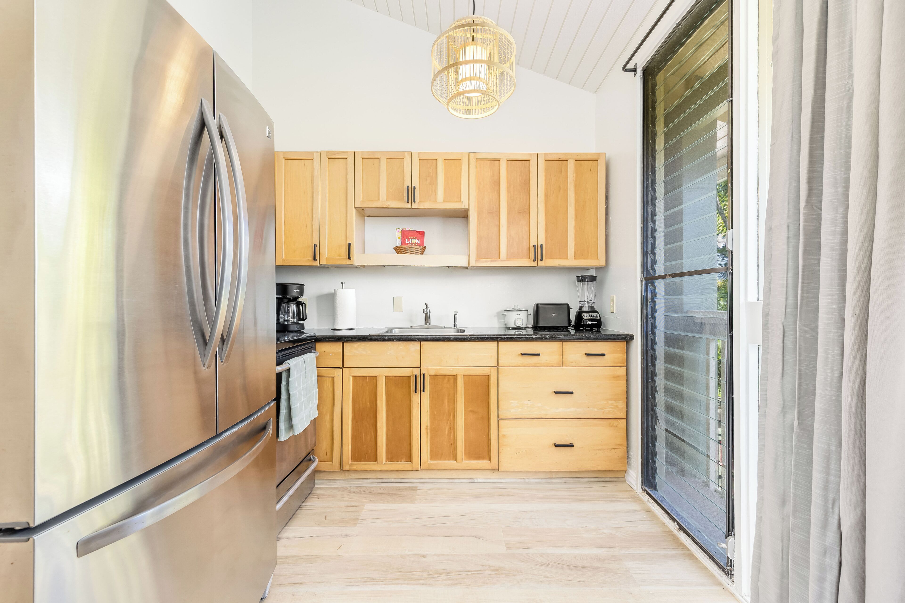 A modern kitchen with wooden cabinets, a stainless steel refrigerator, and a sliding glass door to the outdoors.