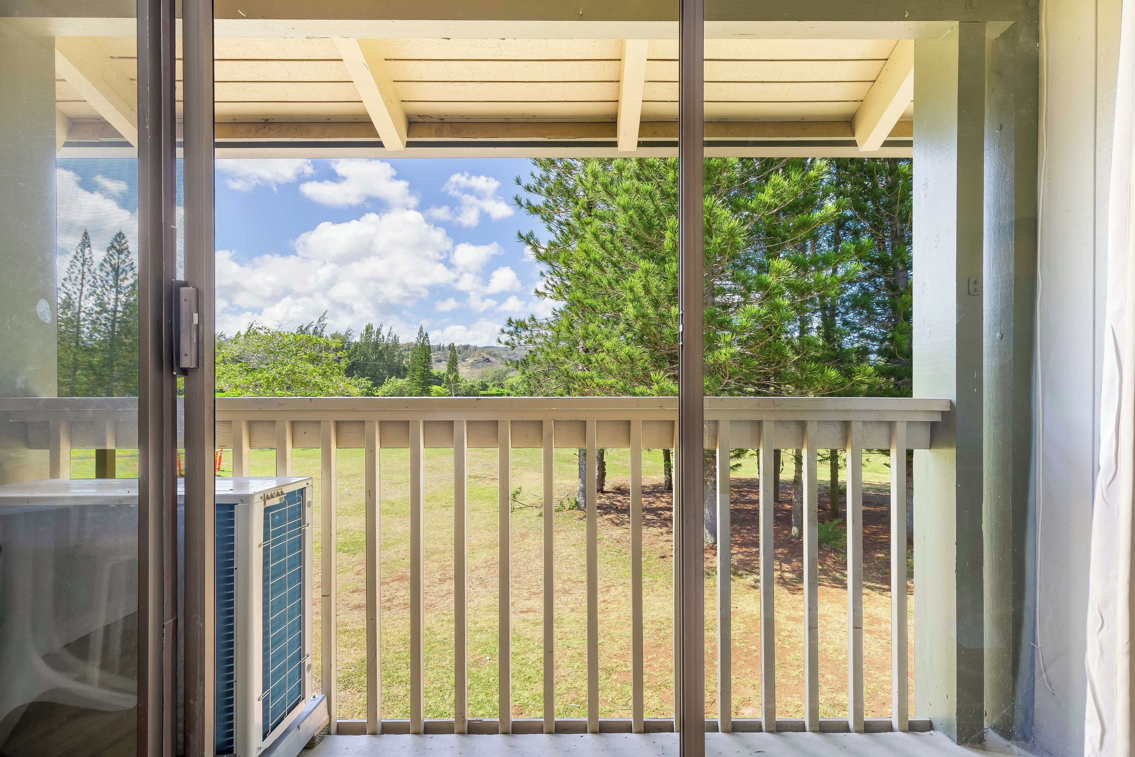 Ein Balkon mit Blick auf einen Rasen und Bäume, einer Holzpergola und einer großen Klimaanlage.