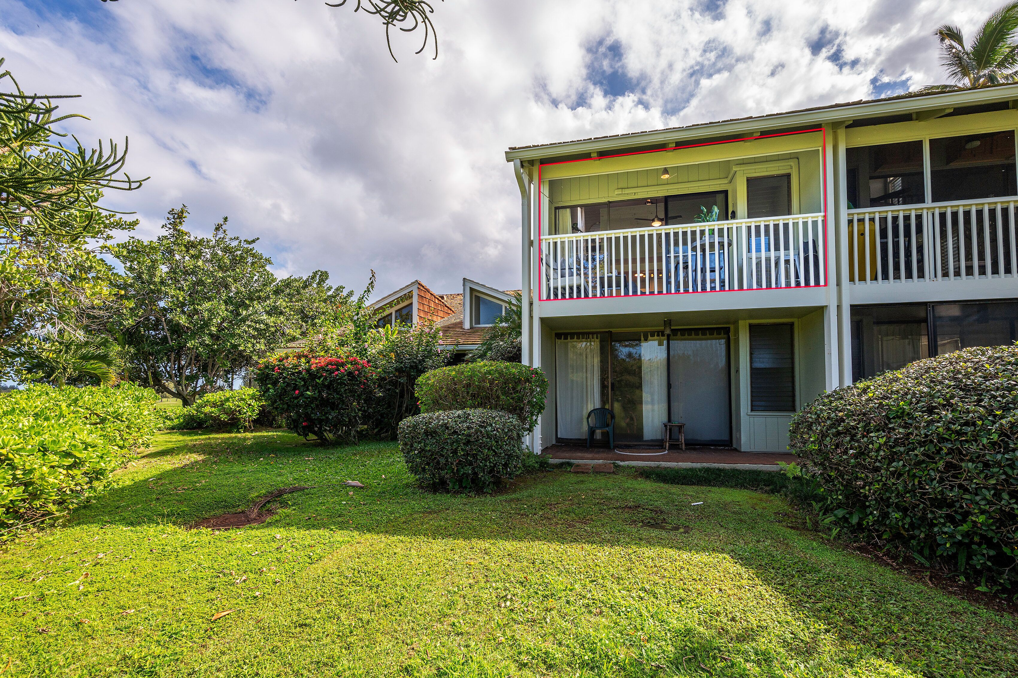 A two-story building with a balcony, surrounded by well-maintained greenery and a clear sky.