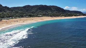A beach with clear turquoise waters and a sandy shore, surrounded by lush green hills.