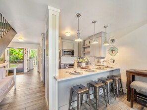 A modern kitchen with stainless steel appliances, a central island with bar stools, and pendant lighting. - Exclusive Golf Course Front Kuilima West by Beach W/parking & Great Amenities (Kahuku)