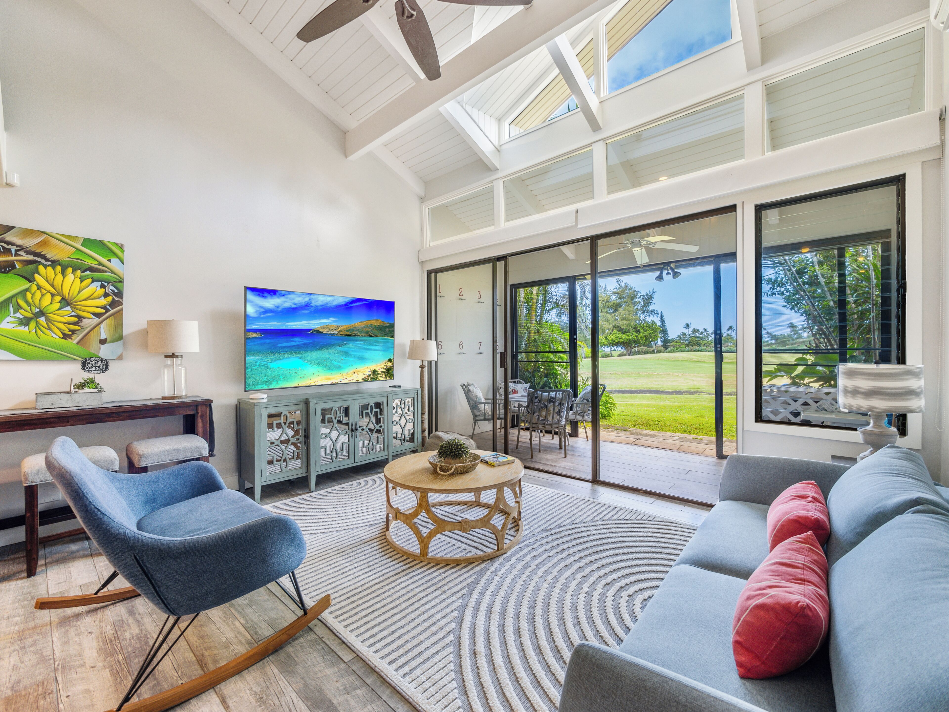 Amplia sala de estar con un televisor de pantalla plana grande, asientos cómodos y vista a un jardín exuberante a través de puertas correderas de vidrio.