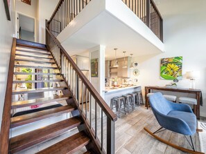 Um interior moderno com escada de madeira, área de cozinha e espaço de estar com uma cadeira de balanço.