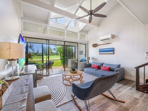 Sala de estar moderna com sofá, cadeiras, mesa de centro e vista para um jardim através de portas de vidro.