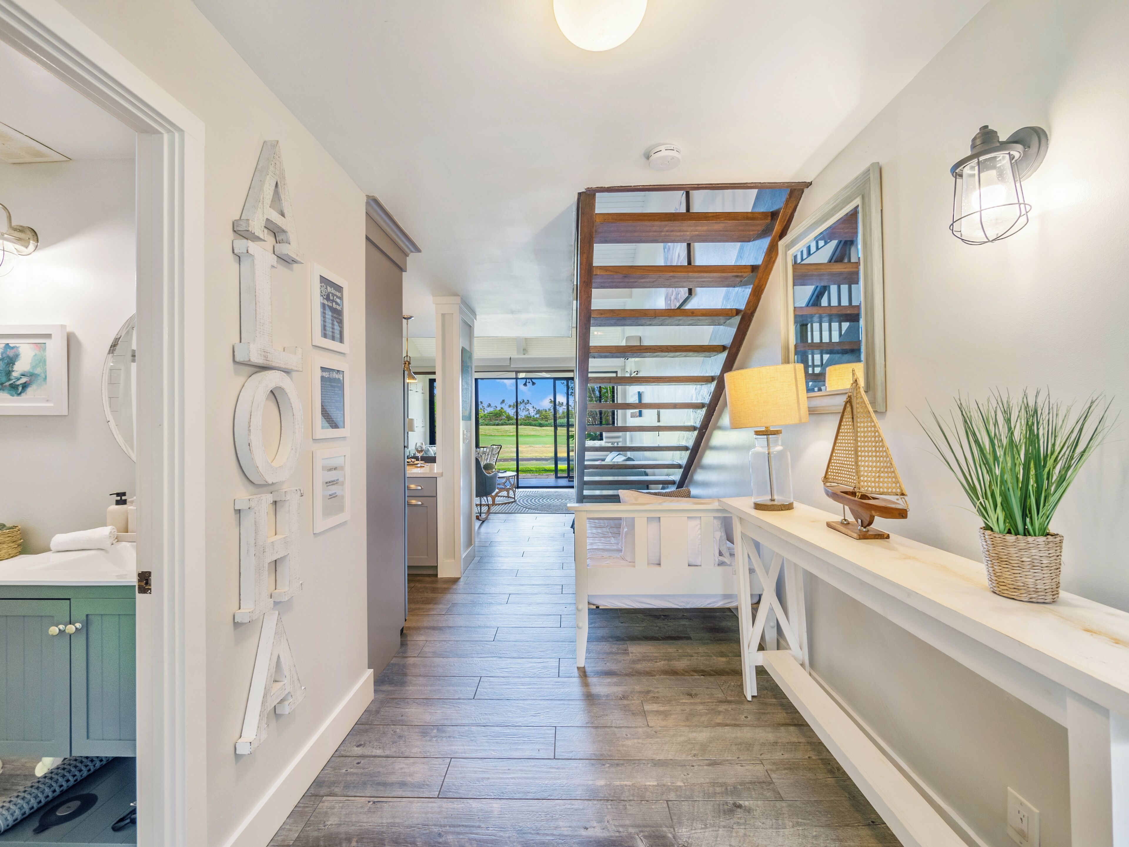 A hallway with a wooden staircase, a white console table with a lamp, and a view of a green landscape through the glass door.