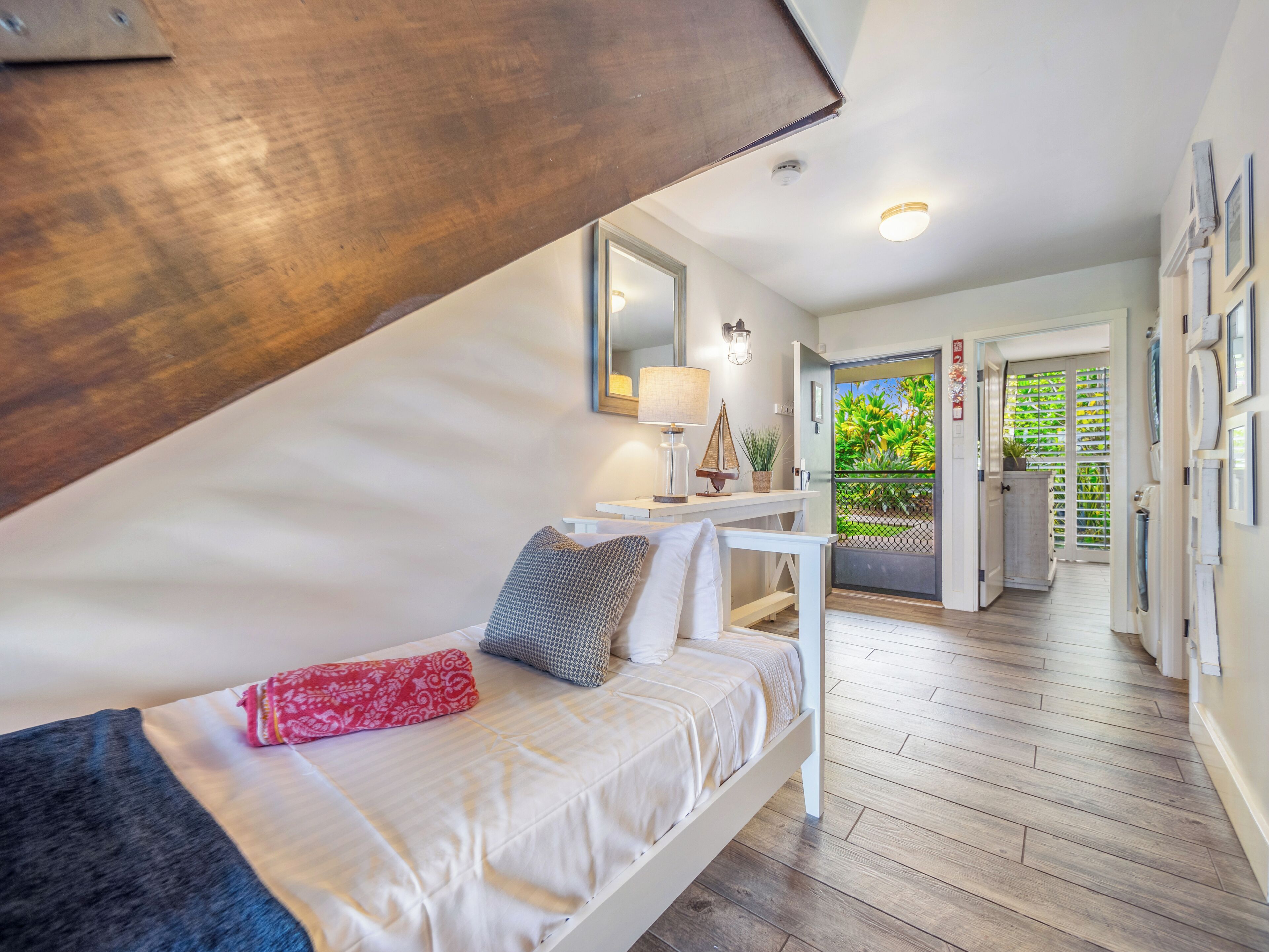 A bedroom with a bed, bedside table, lamp, and a view of the outside.