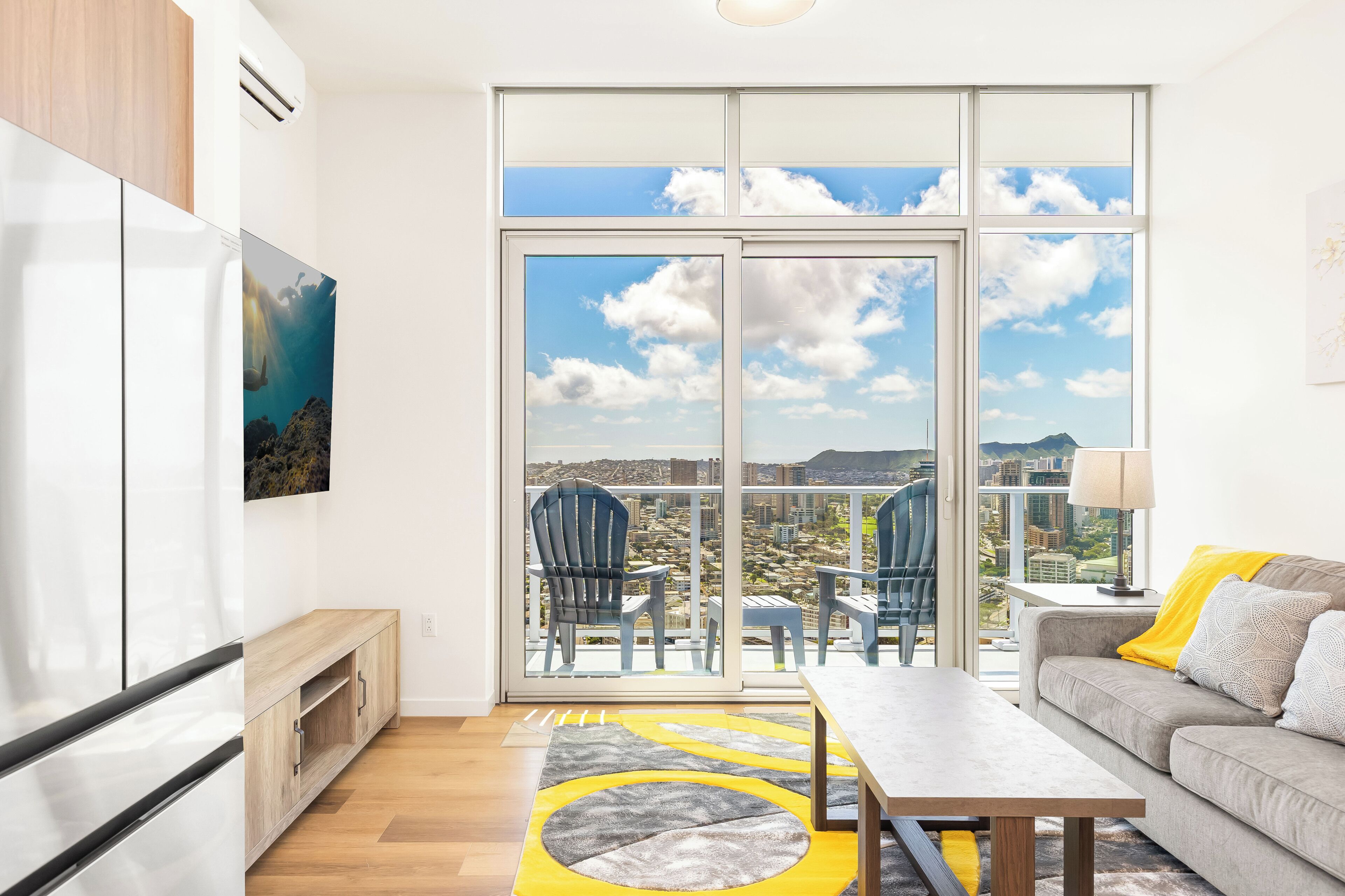 Ein modernes Wohnzimmer mit einem großen Schiebeglasfenster, das auf einen Balkon mit Blick auf die Stadt führt.