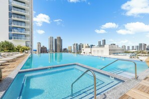 Ein Pool auf dem Dach mit Blick auf die Skyline der Stadt, ein Holzterrasse und ein Hochhaus mit Balkonen.