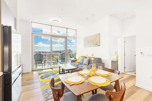 Ein modernes Wohnzimmer mit Esstisch für vier Personen, einer Couch und einem großen Fenster mit Blick auf die Stadt.