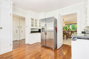 A modern kitchen with white cabinetry, a stainless steel refrigerator, and a wooden floor.