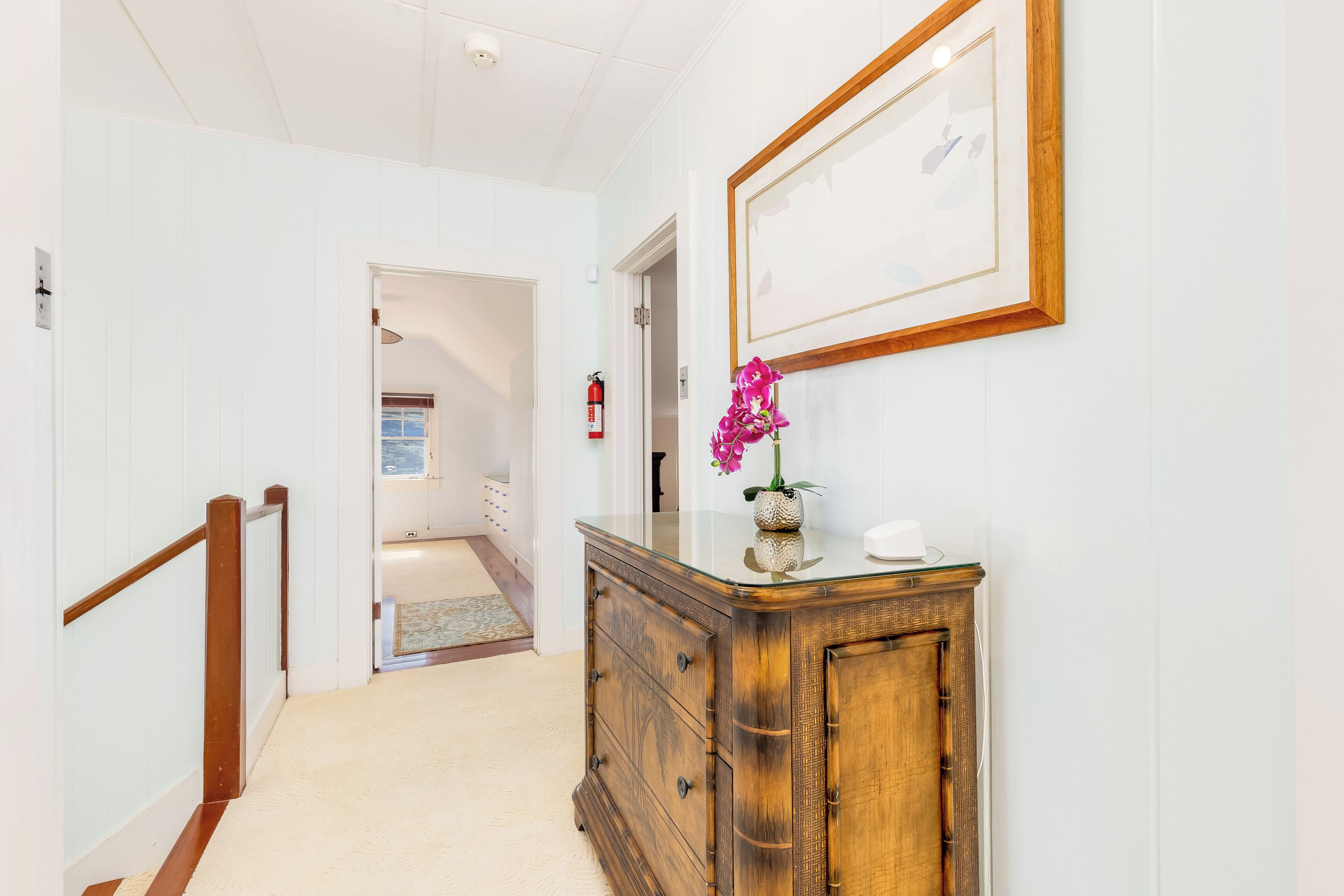 A hallway with a wooden cabinet, a framed picture, and a fire extinguisher.