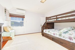 A bedroom with a bunk bed, a desk with a chair, a window with blinds, and a door.