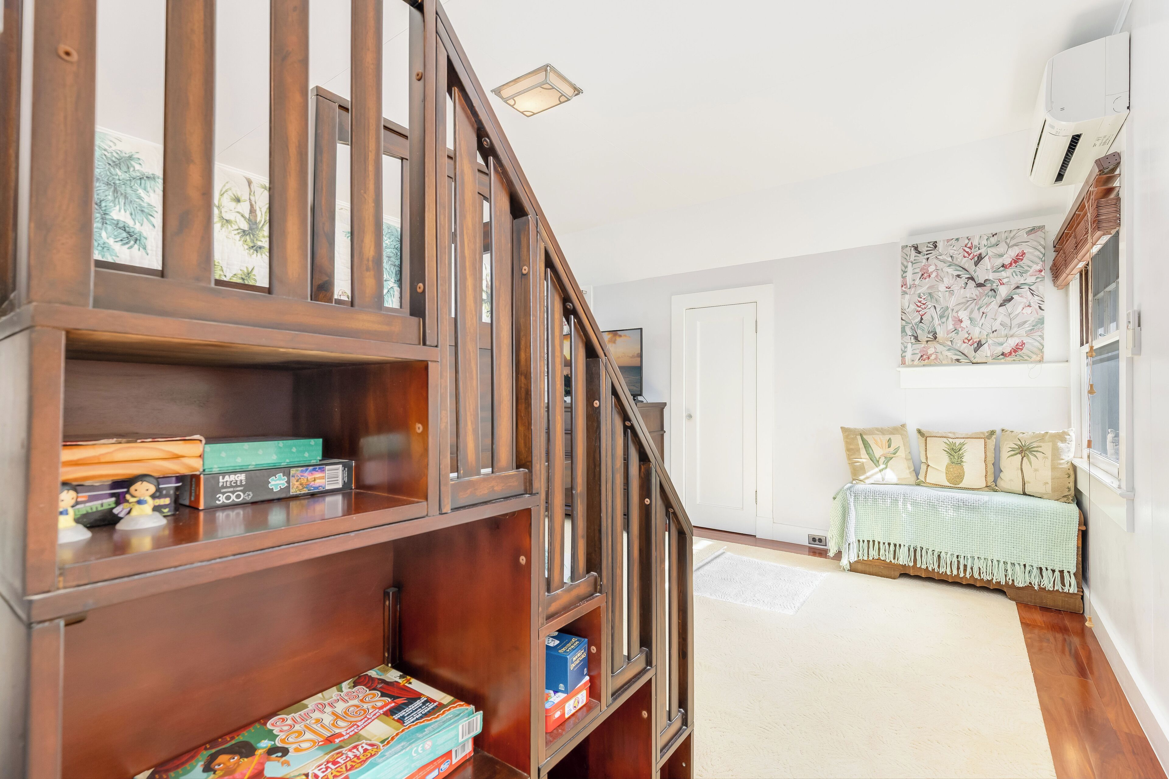 Eine Holztreppe führt zu einem Zimmer mit einem Bett, einem Bücherregal und einer Wand mit einem Blumenbild.