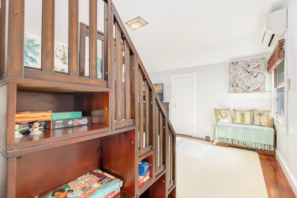 A wooden staircase leading to a room with a bed, a bookshelf, and a wall with a floral painting.