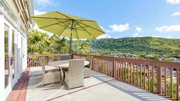 A patio with wicker furniture and a large umbrella, overlooking a lush green landscape and a distant town.