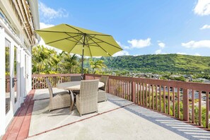 A patio with wicker furniture and a large umbrella, overlooking a lush green landscape and a distant town.