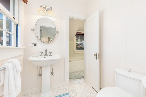 A bathroom with a white sink, mirror, and toilet. There is a towel rack with a towel hanging on it.