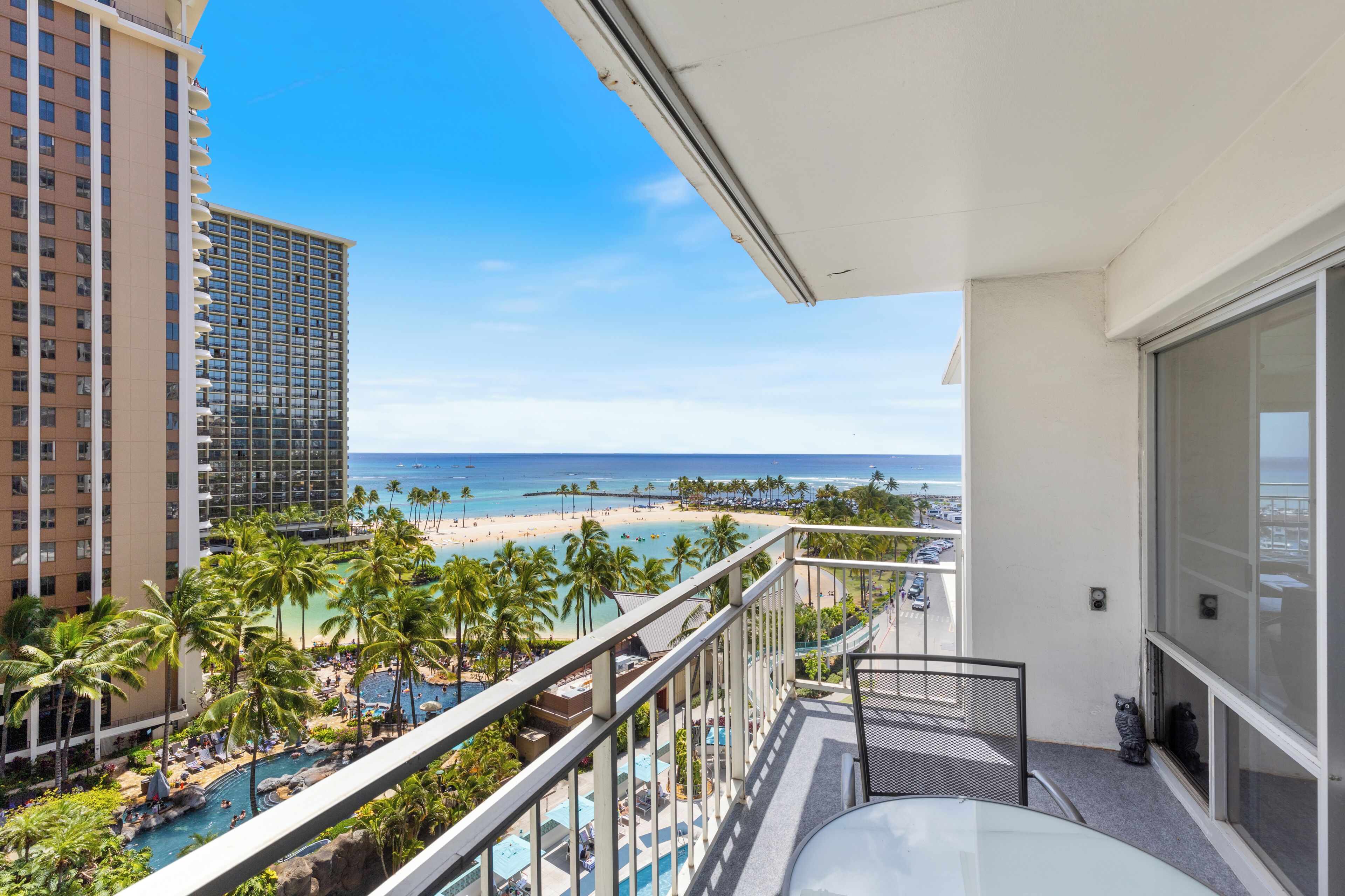 A balcony with a view of a beach, pool, and tall buildings.
