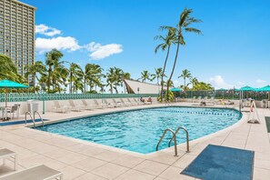 A pool area with lounge chairs and umbrellas, surrounded by palm trees and a tall building. - Ilikai Hotel Condo With Ocean, Lagoon & Fireworks Views (Honolulu)